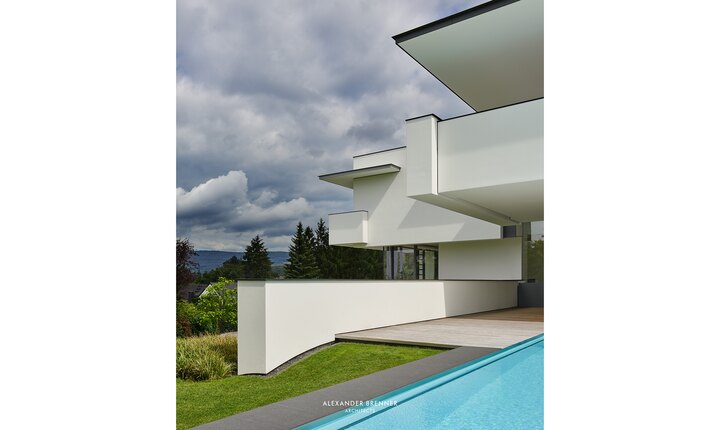 Die hell verputzte Beton­fassade im Kontrast zum Grün der angrenzenden Natur.   Foto: © Alexander Brenner Architects